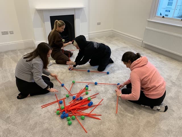 Trainees engaged in a team-building exercise with construction sticks at a Cuckmere Training session